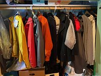 Full view of all jackets and knitwear on hangers on a rod including red, orange, black, grey jackets and knit sweaters.