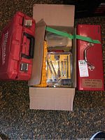 Photo showing a red Milwaukee plastic toolbox, a cardboard box containing various drill bits and tool accessories, and a red metal toolbox labeled for screwdrivers, allen keys and staplers.