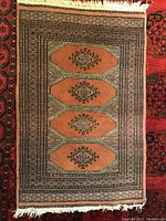 Photo of the larger rug showing geometric motifs in orange tones with fringed edge