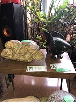 Both sculptures displayed on wooden surface; greenstone ptarmigan next to tan Turtle Legend carving