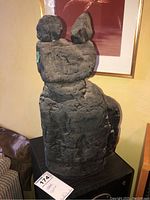 View of abstract stone-like statue showing front and side angles with rough texture and carved details