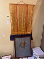 Photo of the two items in the lot: a hanging fabric textile and a framed circular artwork leaning against the wall.