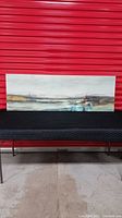 Printed canvas abstract landscape featuring greens, gold, blues, gold, black and some red, signed and no frame, displayed on a black surface with red background.