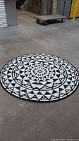 Photo showing the full circular black and white outdoor carpet on concrete floor with its bold modern geometric pattern.