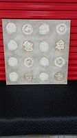 Front view of square canvas artwork showing 16 textured circular motifs on gray background with silver and white details.