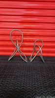 Pair of modern sculptures shown from front, placed side by side on black padded surface in front of red corrugated backdrop.