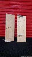 Two raw wood wall shelves with visible wood grain photographed side by side against a red background and black surface