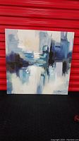 Front view of the square abstract canvas painting showing blues, mauve, white, and black colors with artist's signature in the corner.