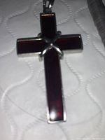 Close-up of cross pendant necklace with red stone inlay and silver 'X' overlay.
