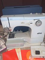 Front view of Elna SU 62C machine with blue carrying case behind