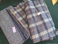Large cuts of folded fabric displayed on a dark surface showing plaid and tweed fabrics.