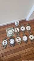 Lot arranged on wooden floor showing nine ornate faux mother of pearl and brass tone metal switch plates and a small white stone keepsake box.