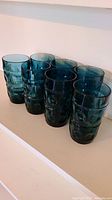 Seven cobalt blue tinted, textured King's Crown pattern glass tumblers arranged side by side.