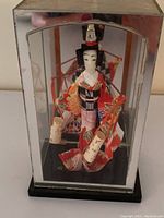 Full view of the Geisha figurine inside the plastic display case showing the entire figure and case dimensions.