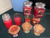 Photo of 7 scented jar candles in various jars including square and cylindrical ones with red, orange and beige wax.