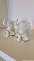 Two ivory ceramic elephant figurines with raised trunks and gold accents on the feet and tusks.