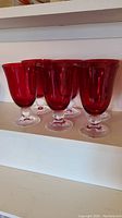 Photo showing six ruby red Lenox glasses with clear stems and bases on a shelf