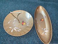 Two mid-century modern hostess serving pieces with brass handles, swirling base paint, gold tone design, and butterfly motifs.