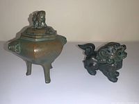 Front view of three-legged hexagonal urn with lid and lion-shaped incense burner side by side on flat surface.