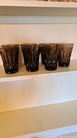 Four of the seven smoke glass tumblers shown on a shelf to display their consistent shape and color