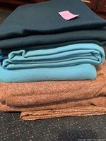 Five folded fabric pieces stacked including dark green Pendleton fabric, blue and teal fabrics, and two brownish fabric pieces.