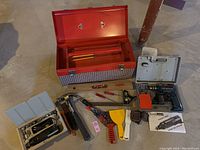Open red metal toolbox with removable tray visible, surrounded by hand tools and two electric drills with cases.