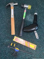 Five hand tools laid out on a carpet: claw hammer, rubber mallet, manual drill, clamp, and Master Sharpener package.