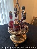 Silver plate castor set with ruby cut-to-clear glass bottles displayed on ornate circular stand with handle