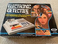 Photo of the Electronic Detective game box showing the product name, a picture of the game unit, and stylized art of characters around a question mark. The box highlights the computerized nature of the who-done-it game and the 130,000 murder mysteries included.