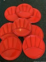 Top-down view of eight red enamel metal lunch plates showing their divided compartments and glossy finish.