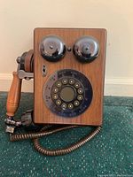 Front view of the vintage wooden wall-mounted telephone showing the rotary dial, two metal bells, and wooden casing.