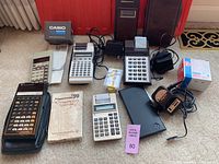 Photo showing the assortment of vintage calculators including TI Programmable 59, Canon Pocket Rider TP 10, Casio ML 90, TI 5025, and accessories such as chargers and carrying cases.