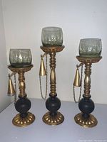 Full view of the three wood and brass candle holders with round tinted glass votives and attached brass snuffers hanging on chains.