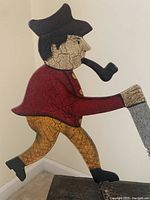Close-up of the wooden folk art figure showing the man sawing with a pipe in mouth, painted with crackled finish