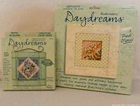 Photo of the front packaging of two Daydreams sewing craft kits by Dimensions, one with floral embroidery and one miniature cross-stitch with a birdhouse.
