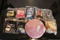 Photo showing eight fast food toys sealed in original plastic packaging along with a pink Spaghetti O's bowl with lid on black surface.
