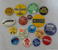 Front view of 17 vintage metal lapel protest pins with various political and social messages, colorful backgrounds and multiple sizes.