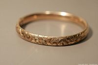 Close-up of the baby bangle showing floral engraving pattern and shiny gold-tone finish.