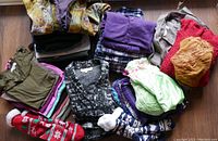 Overhead view of assorted folded clothing including sweaters, pants, socks, and tops laid out on floor