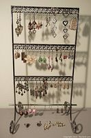 Full view of metal earring display stand holding four rows of assorted pierced earrings and some stud earrings in front.