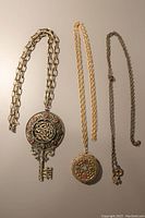 Full view of all three necklaces: large key pendant necklace, round locket necklace, and small key pendant necklace with chains