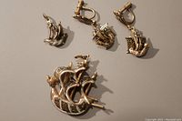Photo showing the full set: large pin, pair of screw-backed earrings, and pendant designed as sailing ships with gold and black tones.