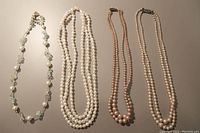 Four short pearl necklaces laid out flat to show styles and length.