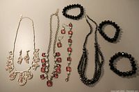 Photo showing all three jewelry sets including necklace and earrings in pink, necklace, earrings, and bracelet in red, and black necklace with three elastic bracelets.