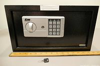 Front view of the black Garrison safe showing keypad, turn handle, keyhole, and placed above a ruler for scale.