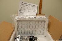 LED grow light panel in original box with instruction sheet, power cord, and hanging hardware visible.