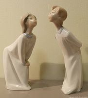 Front view of Lladro boy and girl kissing figurines side by side showing posture and details.