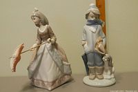 Front view of both porcelain figurines, showcasing boy with dog and girl with parasol.