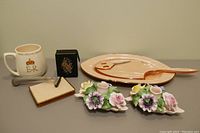 Overview of peach vanity set items, black and rectangular smoke cases, razor, commemorative mug, and flower candle holders.