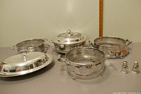 Full lot view showing 3 silver pot holders and 2 covered serving pots, also the salt and pepper shakers visible to the right.